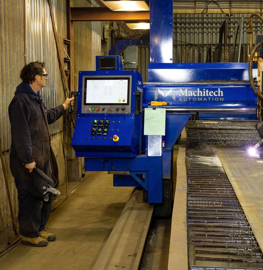 Employé devant une table de coupe avec 1 tête au plasma haute définition 400 AMP, 5 axes. 2 têtes à l'oxycoupage jusqu'à 6'' d'épaisseur"